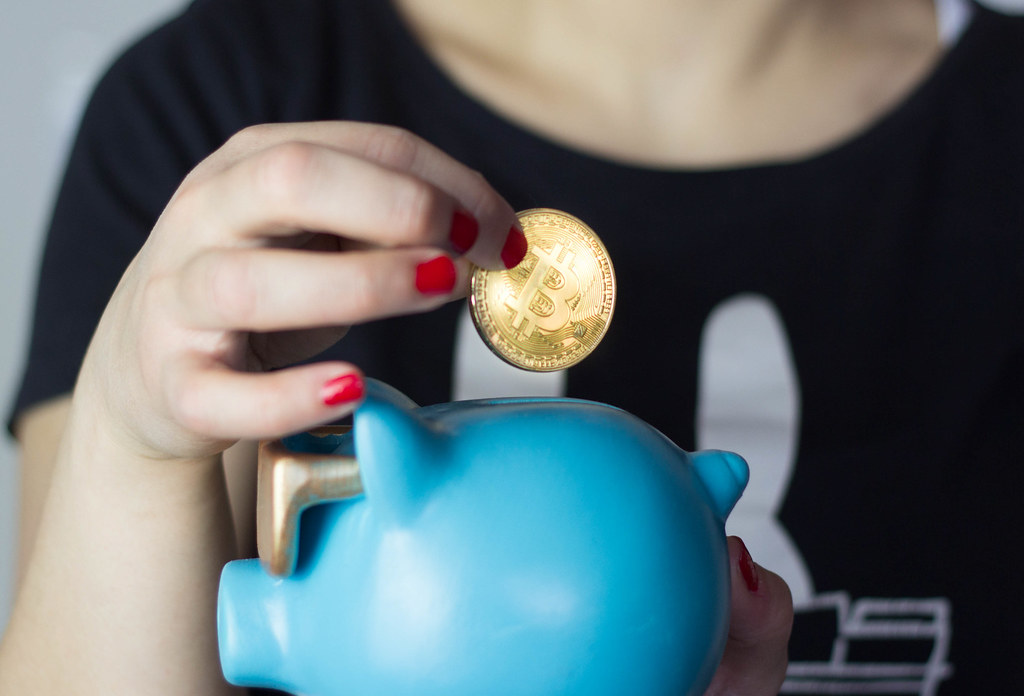 Picture of a hand putting a bitcoin in a piggybank